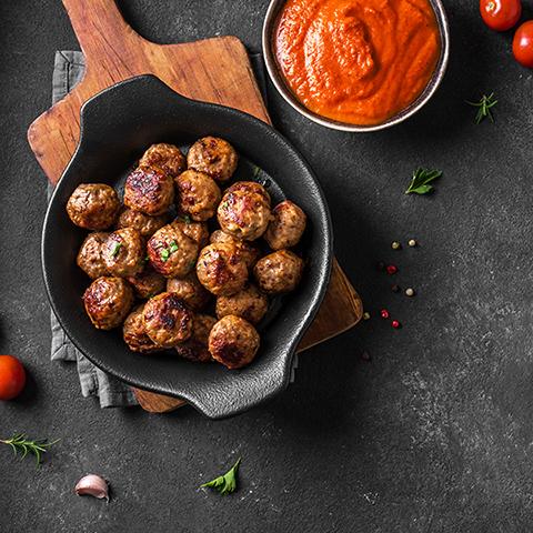 Image of meatballs in skillet and red sauce. 